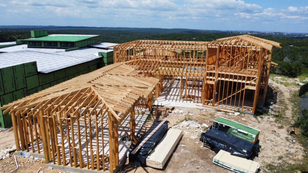 Aerial drone photography of a luxury custom home construction project in Austin Texas featuring wood framing roof truss installation structural development and residential construction progress by a professional custom home builder.